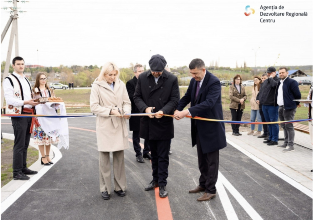Officials cut a ribbon on a newly paved road as onlookers stand nearby; logo of Agenția de Dezvoltare Regională Centru in the corner.