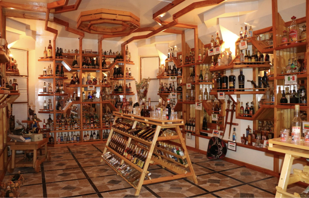 Interior of a wooden liquor shop with shelves full of bottles and a tilted central display rack of bottles.