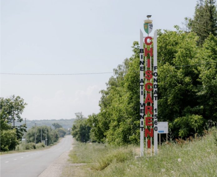 chiscareni Tall white roadside sign with large red vertical letters beside a rural road and green trees.