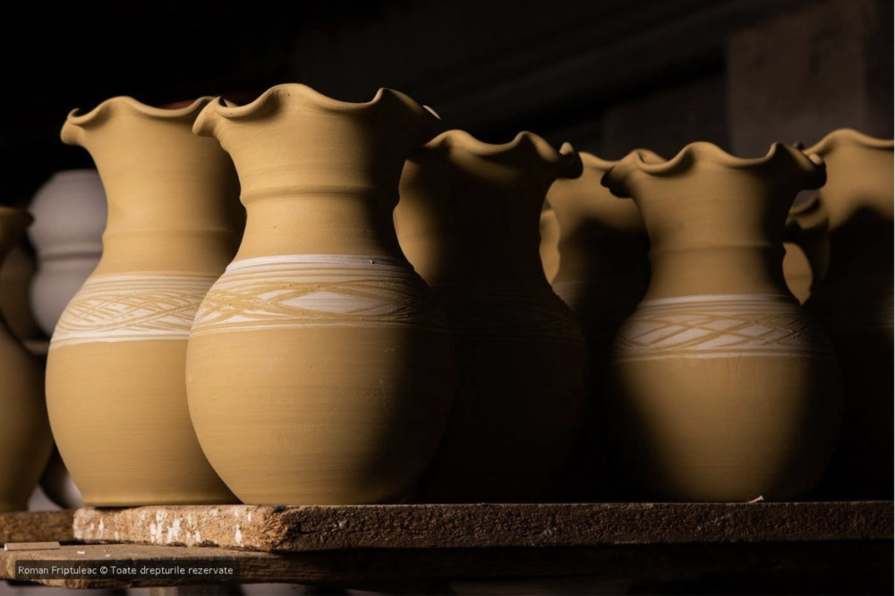 Row of unglazed terracotta vases with decorative bands on a wooden shelf in a pottery workshop.