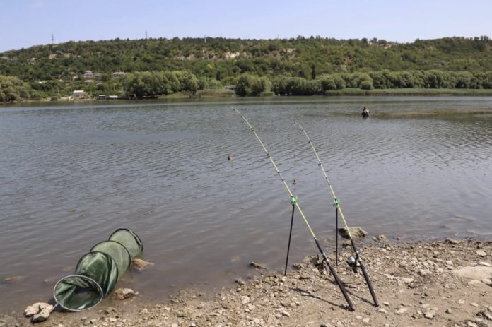 pescari Two fishing rods propped on the rocky lake shore with a green collapsible net nearby in the water.