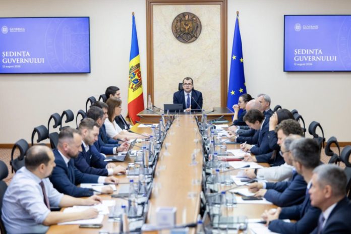 guvern Government officials seated around a long conference table in a formal meeting, Moldova and EU flags behind the central speaker.