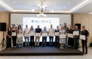 undp-proiect Group of people on a stage holding certificates during an awards ceremony, with a logo backdrop.