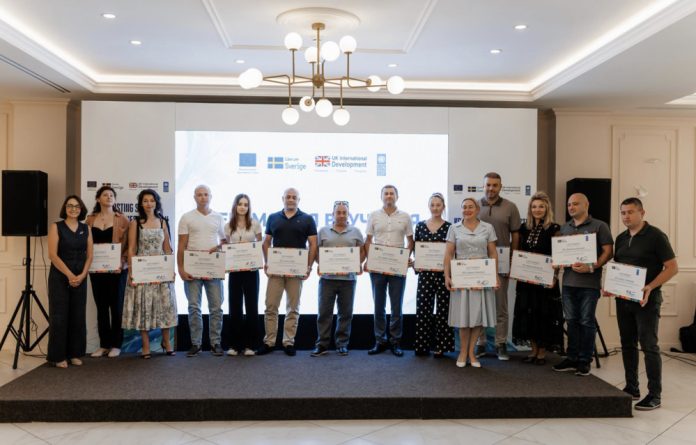 undp-proiect Group of people on a stage holding certificates during an awards ceremony, with a logo backdrop.